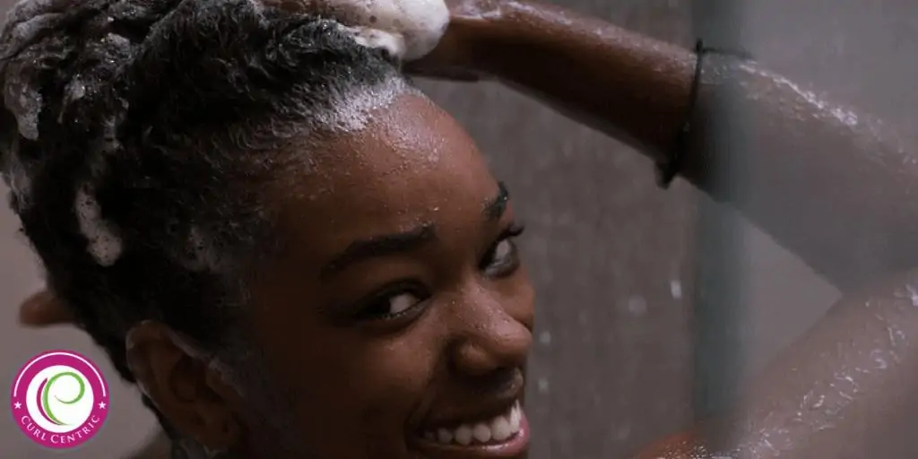 How to Pre-Poo Curly Hair With Olive, Coconut Oil, and More 1 Cute young African American girl using a pre-shampoo treatment on her wet hair to impart extra moisture.