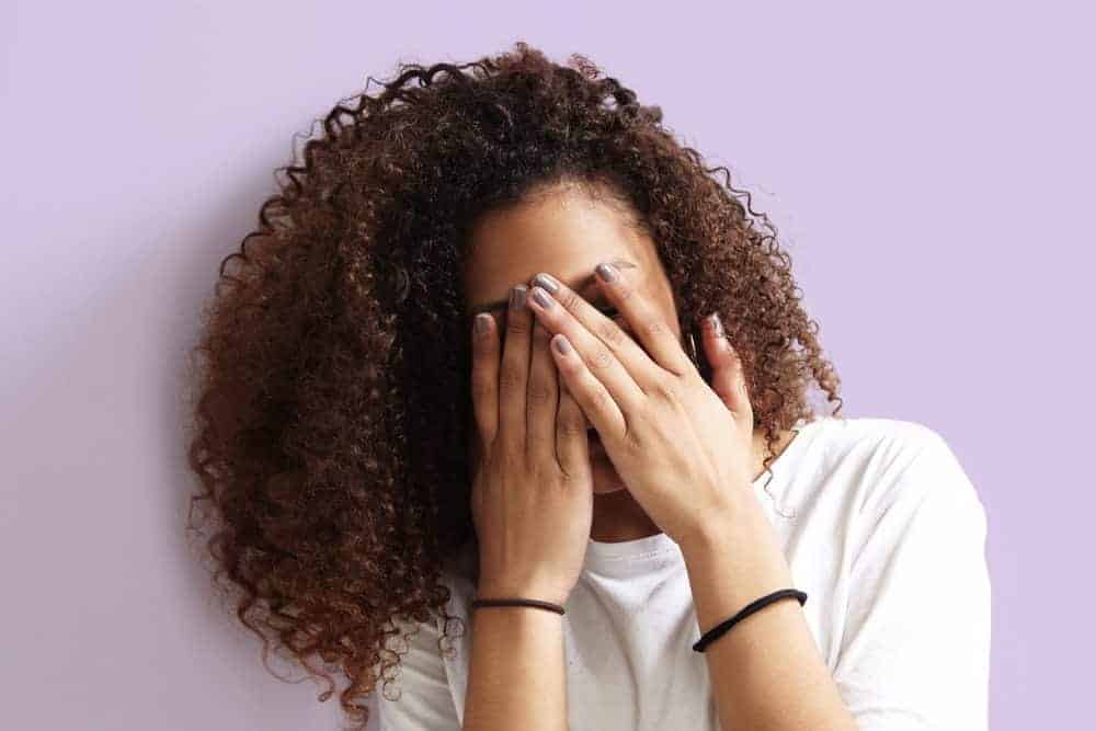 Pretty light skinned African American female with curly hair and purple fingernail polish covering her face.
