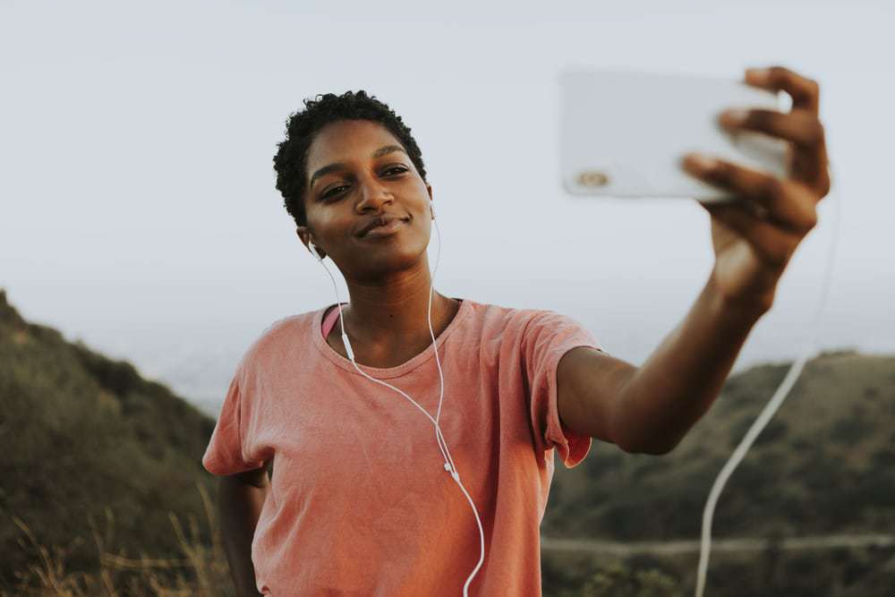 A lady recording a video on her iPhone discussing how you can use a curl sponge to create defined curls.