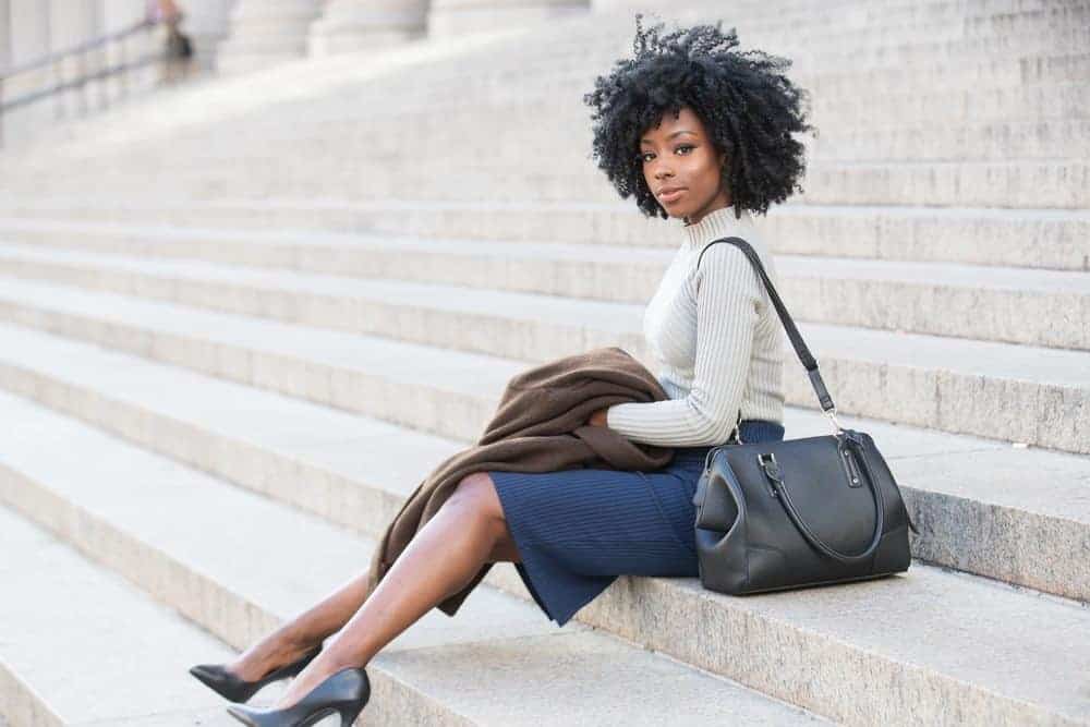 The Best Essential Oils for Hair Growth and Thickness (Our Favorites & DIY Tips) 9 African American female wearing a ribbed sweater, blue skirt, black heals and with beautiful curly hair.