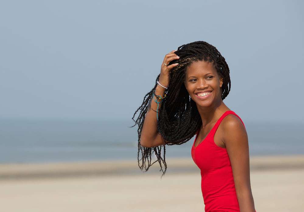 African American women on the beach with a cute red swimsuit wearing black and blonde goddess braids