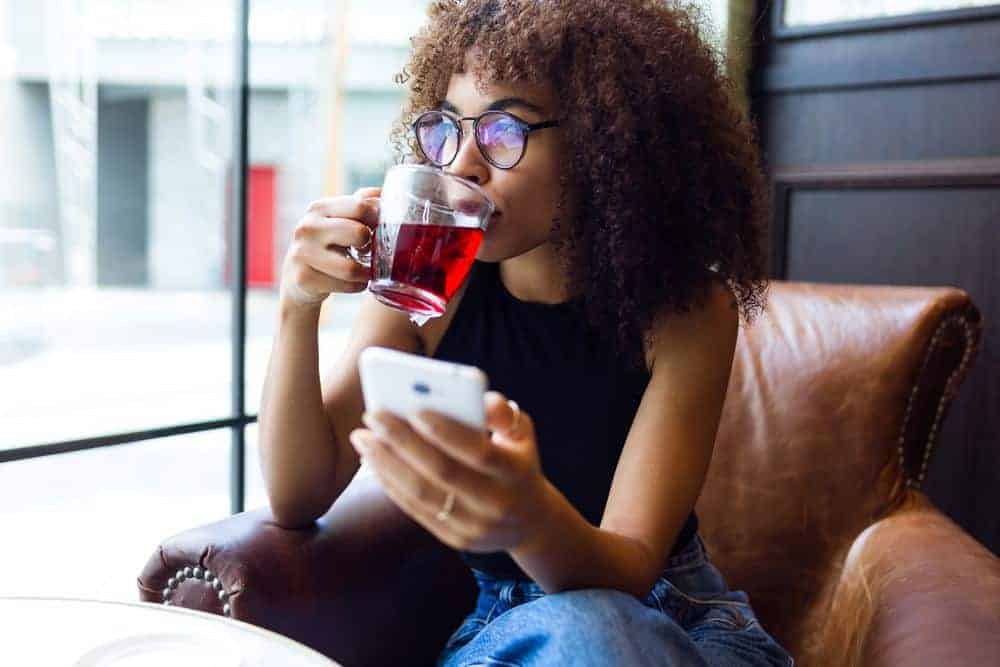 A cute young black girl wearing a wash-n-go styled with natural oils is drinking red tea while relaxing in a coffee shop.