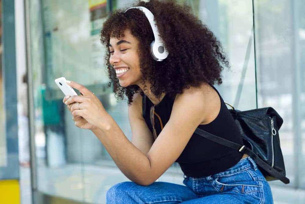 African female with fine hair researching whether you can leave grapeseed oil in thin or fine hair on her phone.