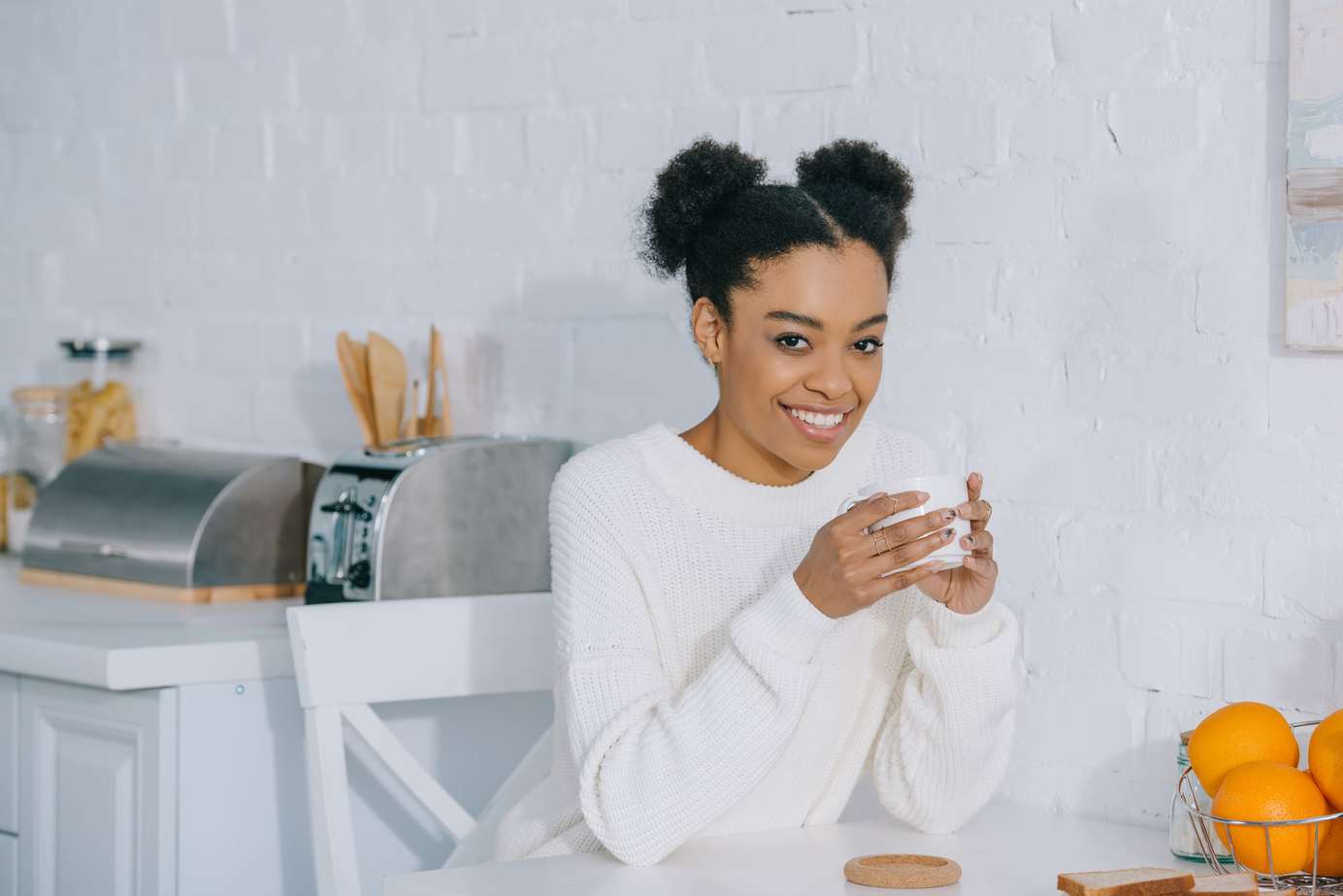 African American lady with natural hair afro puffs drinking coffee wearing a white sweater