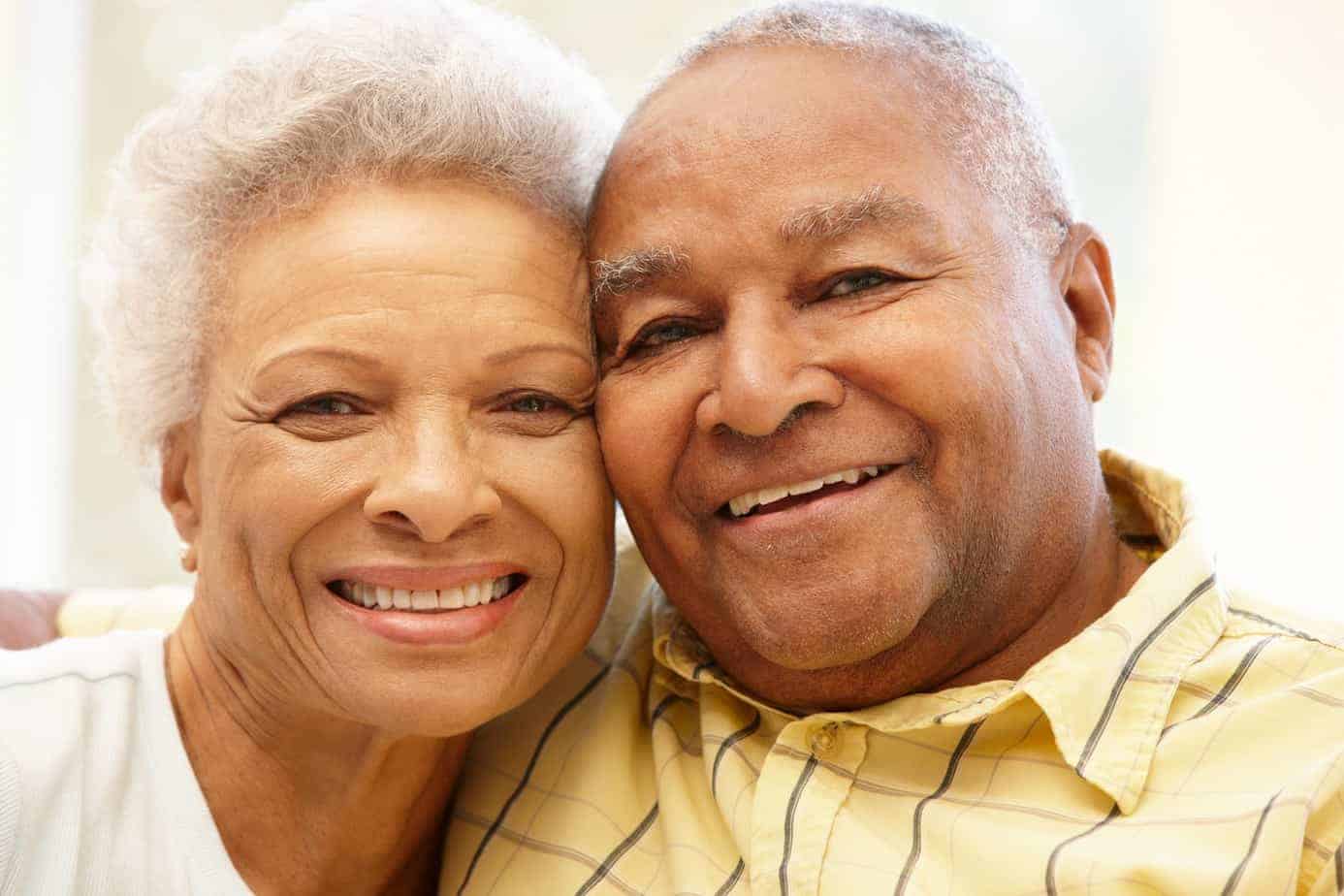 Older black couple, one women and one man smiling and looking directly into the camera.