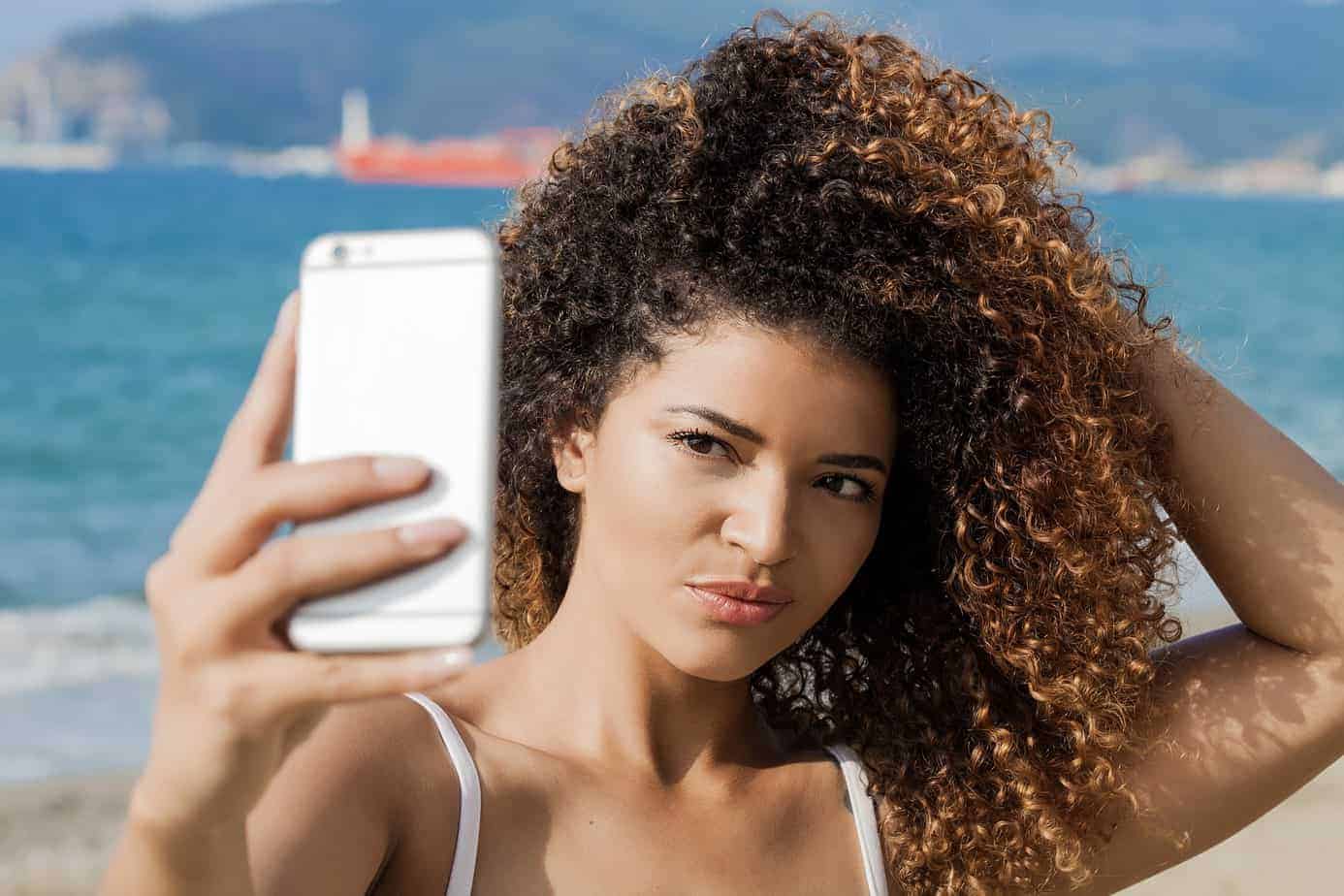 Young, cute woman taking a selfie on the beach with her iPhone after moisturizing her hair with lavender essential oil.