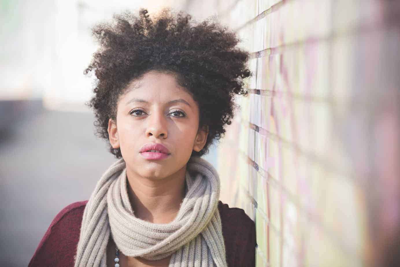 Black female with naturally curly hair wearing a badge scarf and a red sweater.