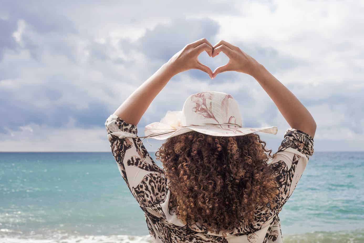 A young black female making a heart symbol with hands with curly hair styled with a lavender hair mask and olive oil.