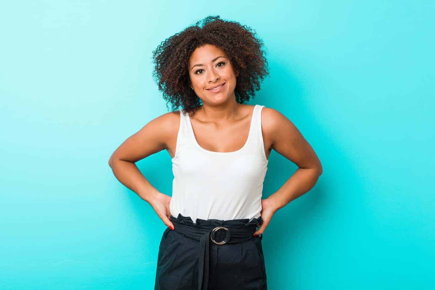 Young African American female smiling while wearing green pants, a white tank top, and spring twists on her own hair.