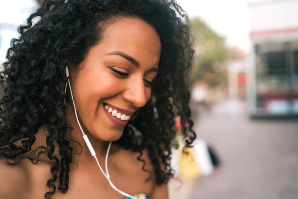Portrait of young mixed African American Latin woman with damaged hair listening to music with iPhone earphones outdoors in the street.
