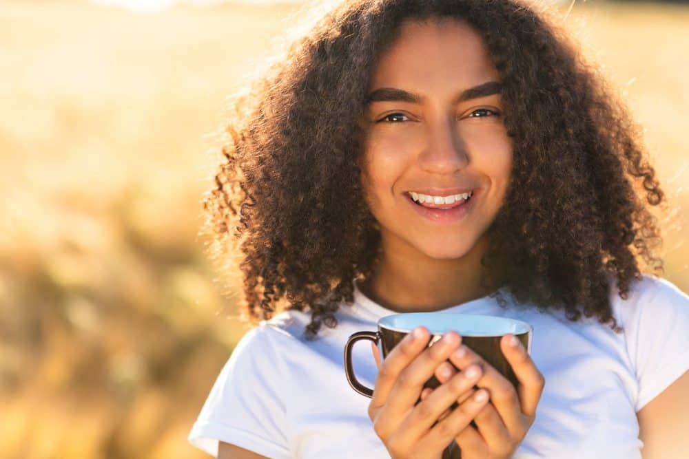 Beautiful mixed race female smiling with perfect teeth wearing a white t-shirt while drinking coffee outdoors.