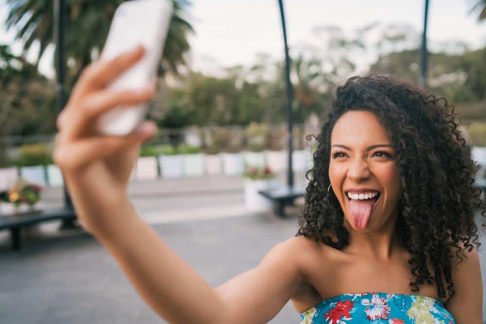 Learn How to Use Almond Oil for Hair Growth, Dandruff, Hair Loss, and Skin Care 9 Young African American Latin woman taking a selfie with mobile phone outdoors in the street.