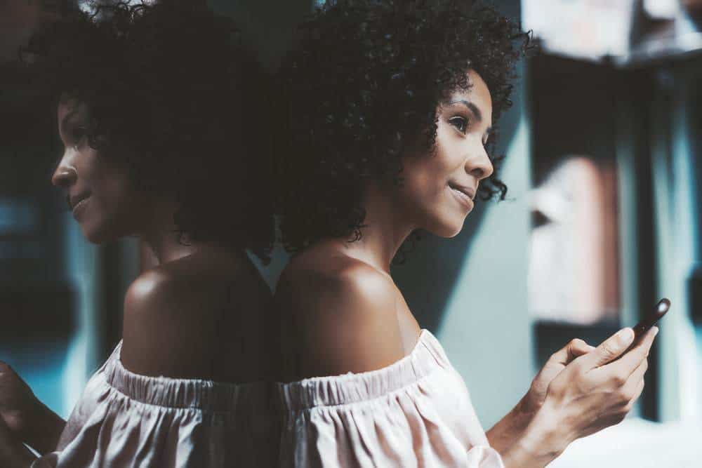 A thoughtful dazzling young biracial female leaning against the mirror wall outdoors.