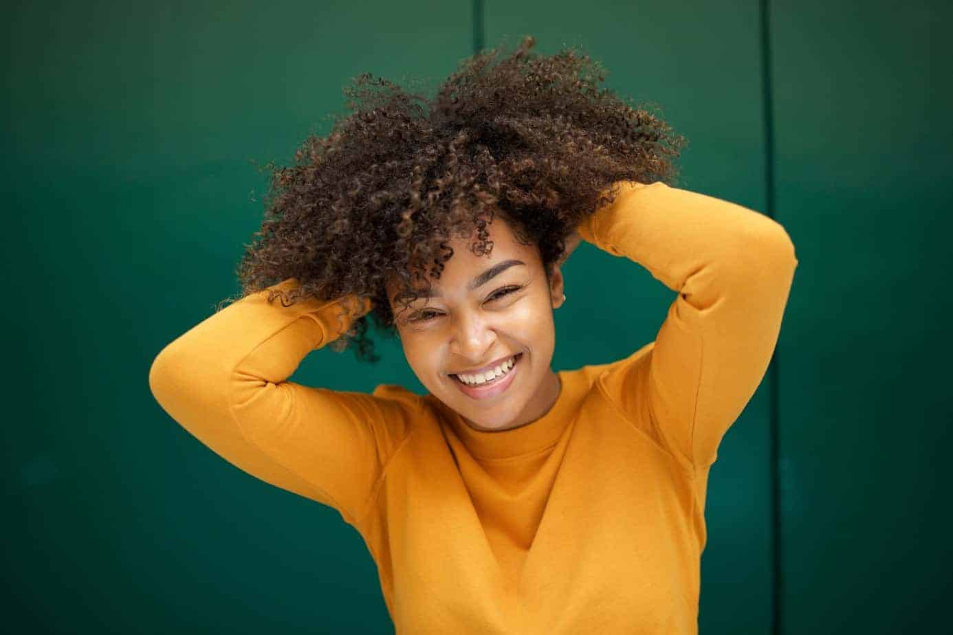 Black female with bouncy curls wearing an orange shirt showing the before and after results of chebe powder.