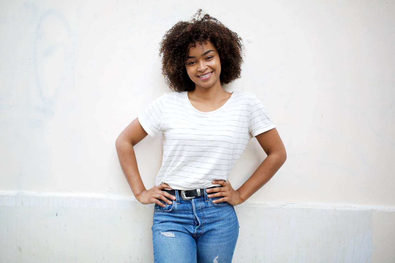 Full body photo of African American girl with medium hair length wearing a striped shirt and jeans.