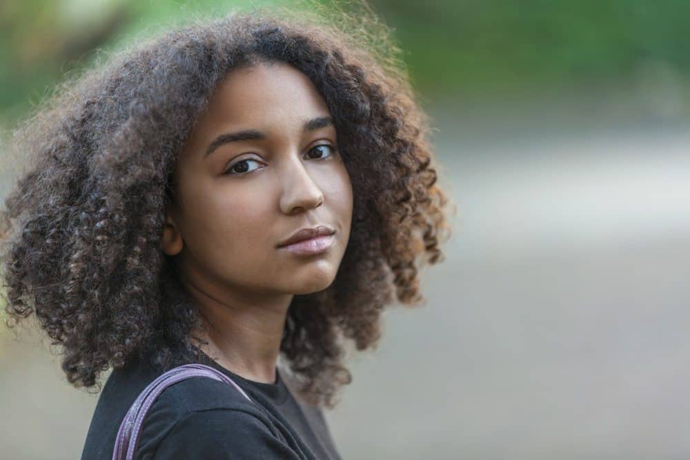 Outdoor portrait of beautiful mixed race African American female with hair that's been treated with coconut oil for hair growth and scalp care.