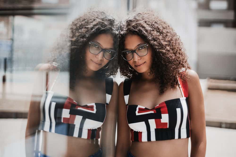 Caucasian woman leaning on a glass wall while wearing a red and black crop top with type 2c wavy hair.