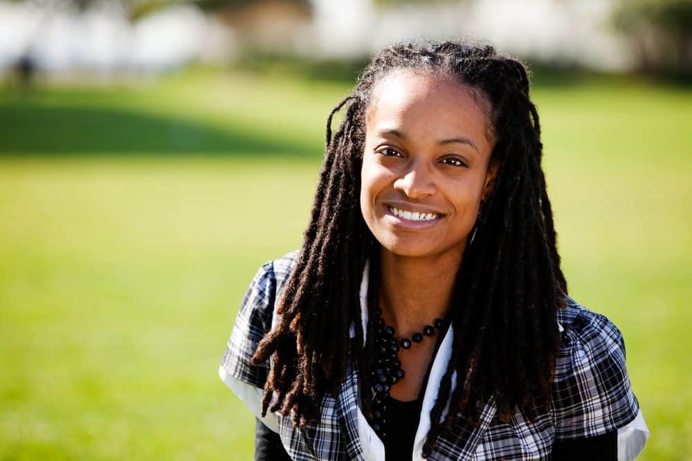 A beautiful African American women with dreadlock extensions, also referred to as loc extensions. She wearing a plaid shirt and black beaded necklace.