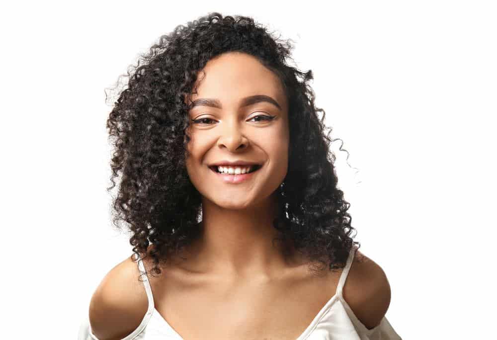 Beautiful African-American woman on white background wearing shoulder cut white top with naturally curly 3a hair type.