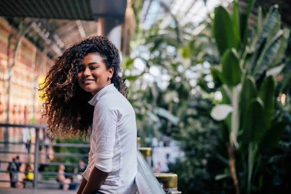 Beautiful girl with curly hair treated with rosemary oil standing outdoors looking at camera.