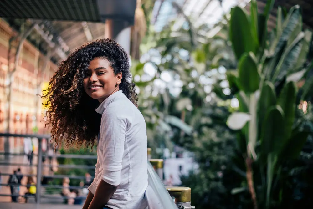 How to Use Thyme Oil for Hair Growth, Stress, Dry Scalp, and More 2 Beautiful girl with curly hair treated with rosemary oil standing outdoors looking at camera.