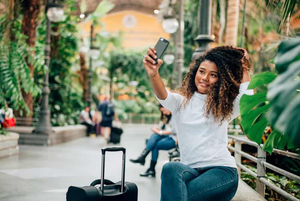 Lovely tourist African American girl taking selfie with thyme oil treated curly hair sitting in the mall. 