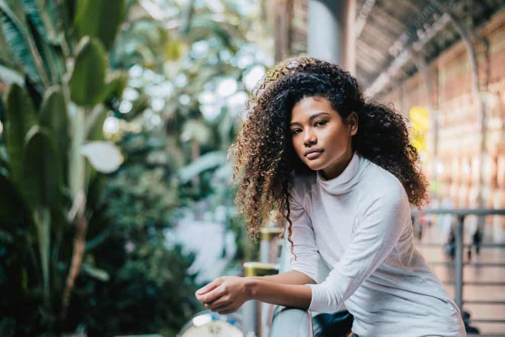 Portrait of young woman with curly afro hair standing against fence in shopping mall.