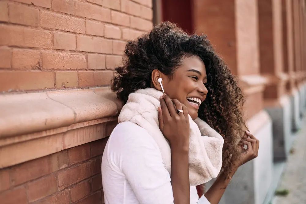 How to Use Thyme Oil for Hair Growth, Stress, Dry Scalp, and More 5 Young beautiful black woman with thyme oil treated hair leaning on a wall outdoors in city street listening music with headphones.