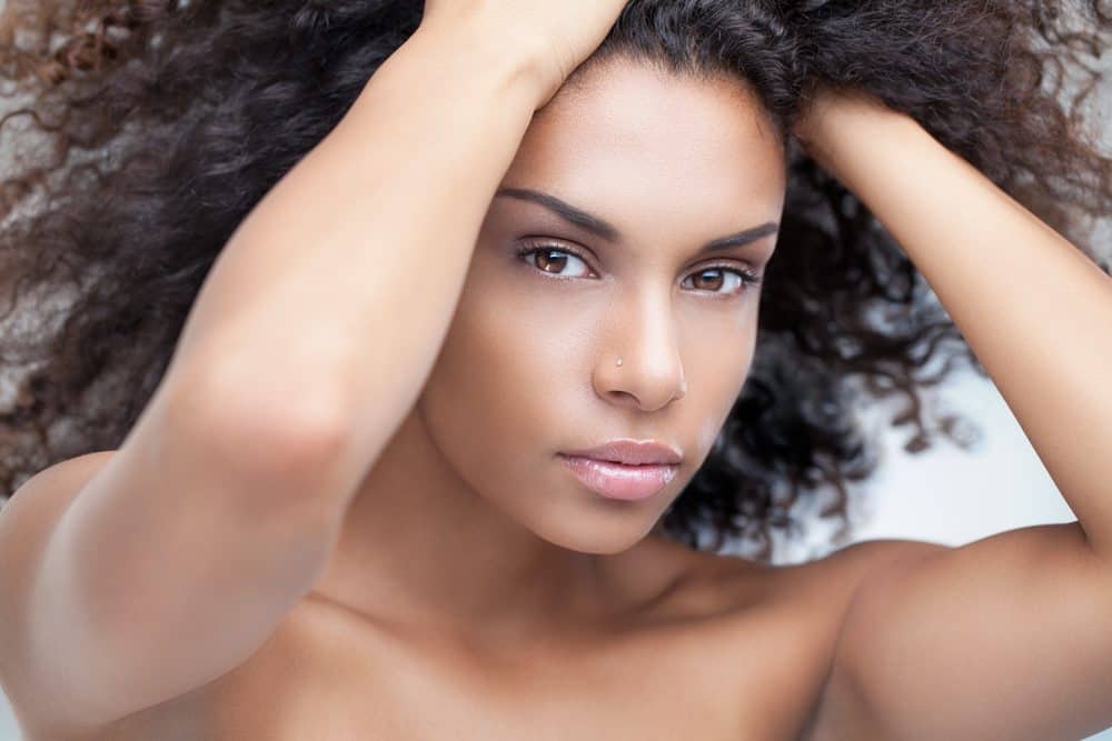 African woman with hands in hair creating a curly ponytail.