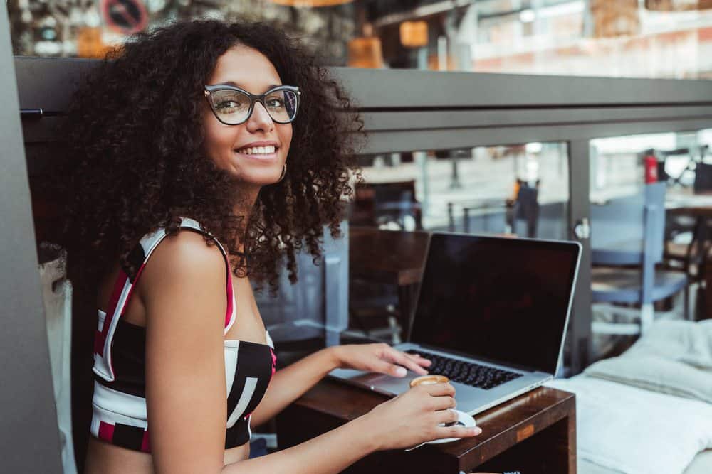 Young Indian businesswoman wearing black glasses in an outdoor restaurant working on content within an Excel spreadsheet.