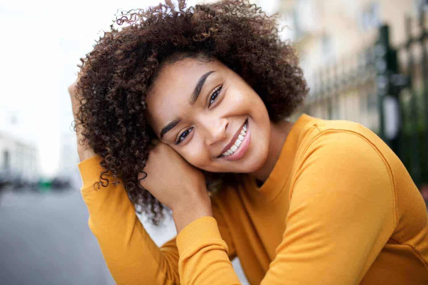 Beautiful young African American woman smiling at the camera with curly hair after using chebe powder for hair growth and length retention.