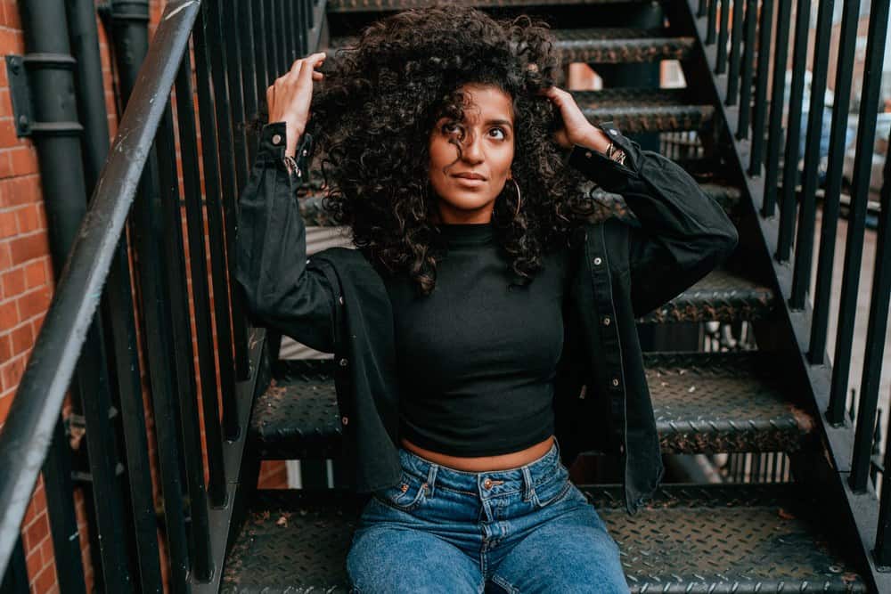 Portrait of charming African American woman with sunflower oil treated curly hair sitting a the stairs of a street corner, intentionally posing outdoors for this photo.