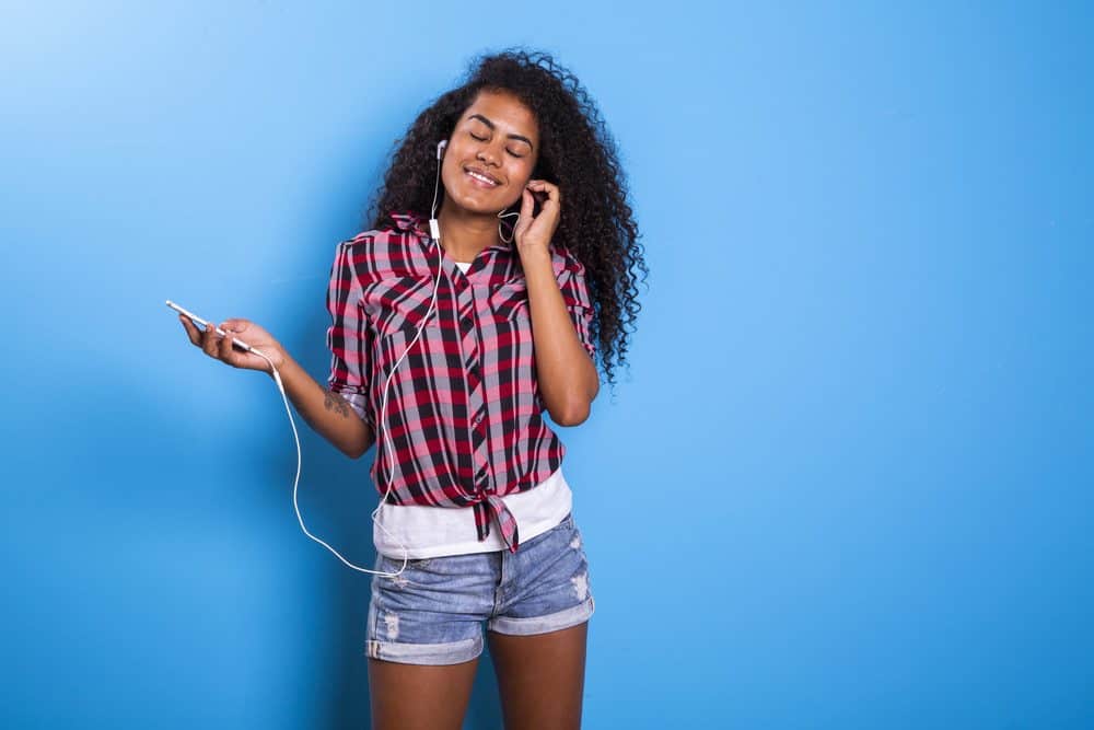 Cute amazing Indian American woman, dancing while listening to ipod music in apple head phones wearing a plaid shirt and blue jean shorts.