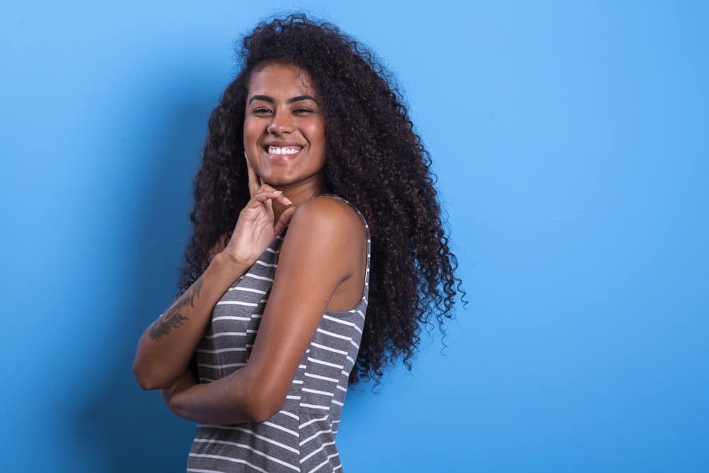 Cute smiling black woman with afro hairstyle on blue background with a dragon tattoo on her right arm.