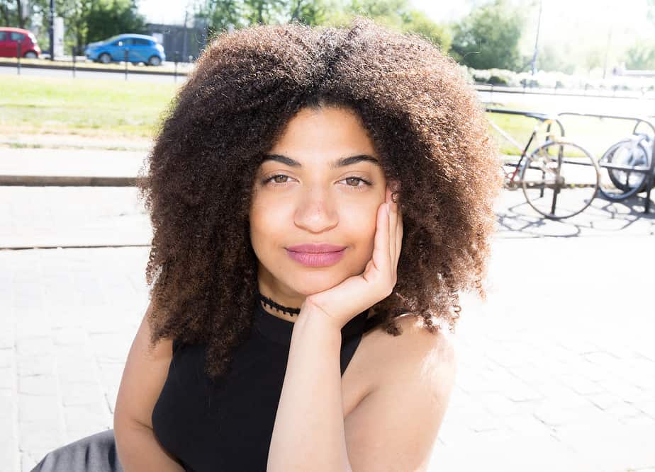 Beautiful mixed-race lady with curly hair sitting on a bench in the center of the city after her hair has been treated with peppermint oil.
