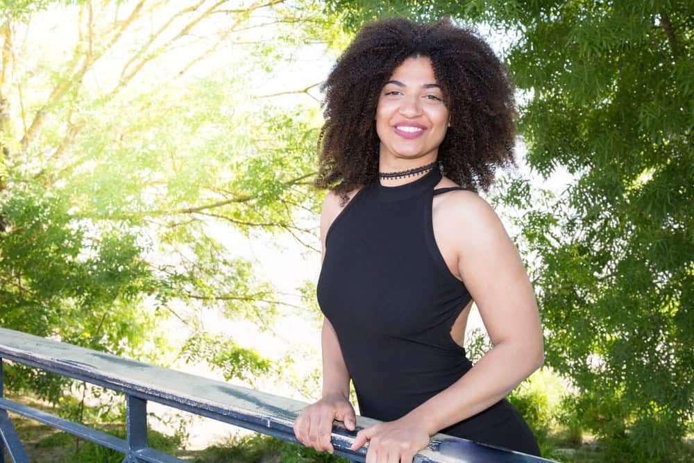 Curly brown girl on a bridge with nice green brushes and trees in the background.