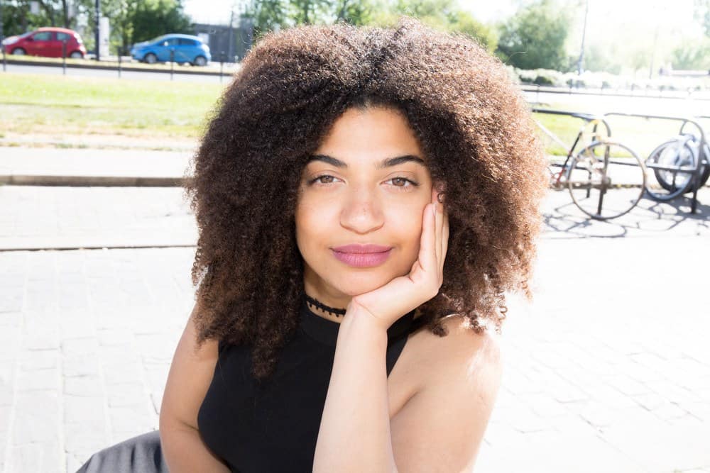 Beautiful mixed race lady with curly hair sitting on a bench in the center of the city after her hair has been treated with peppermint oil.