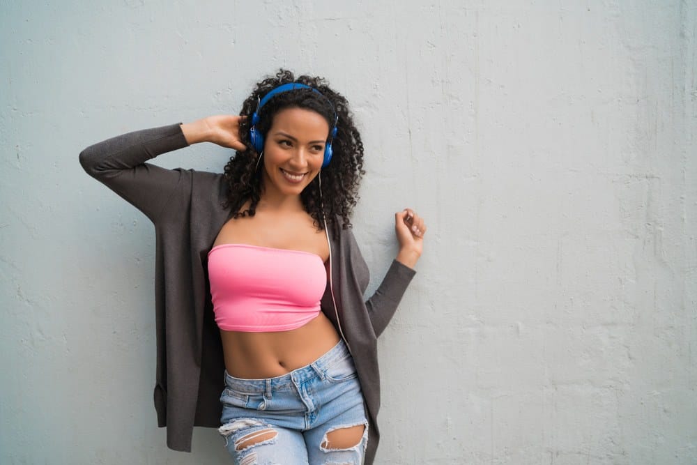 Young Mexican woman enjoying and listening to music with blue headphones and torn blue jeans.