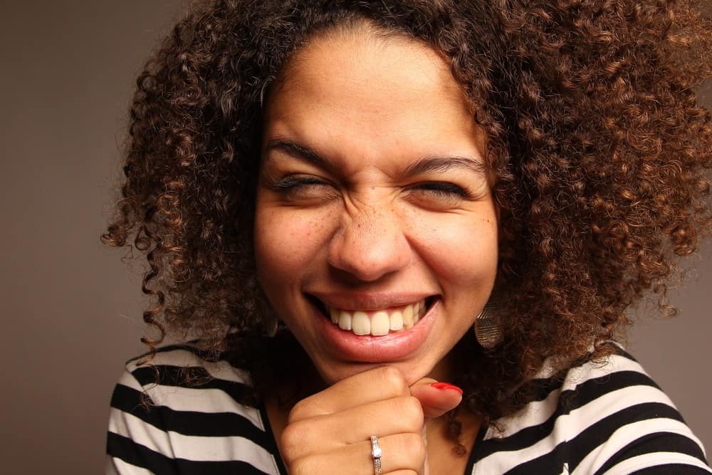 Beautiful black female with naturally curly hair wearing a diamond ring, gold earrings, red fingernail polish and pink lipstick.