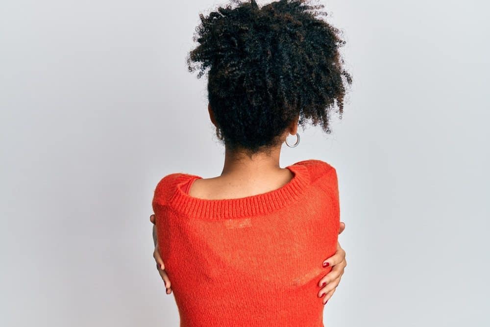 Young African American girl wearing casual clothes hugging herself from the back. She's showing self love and self care.