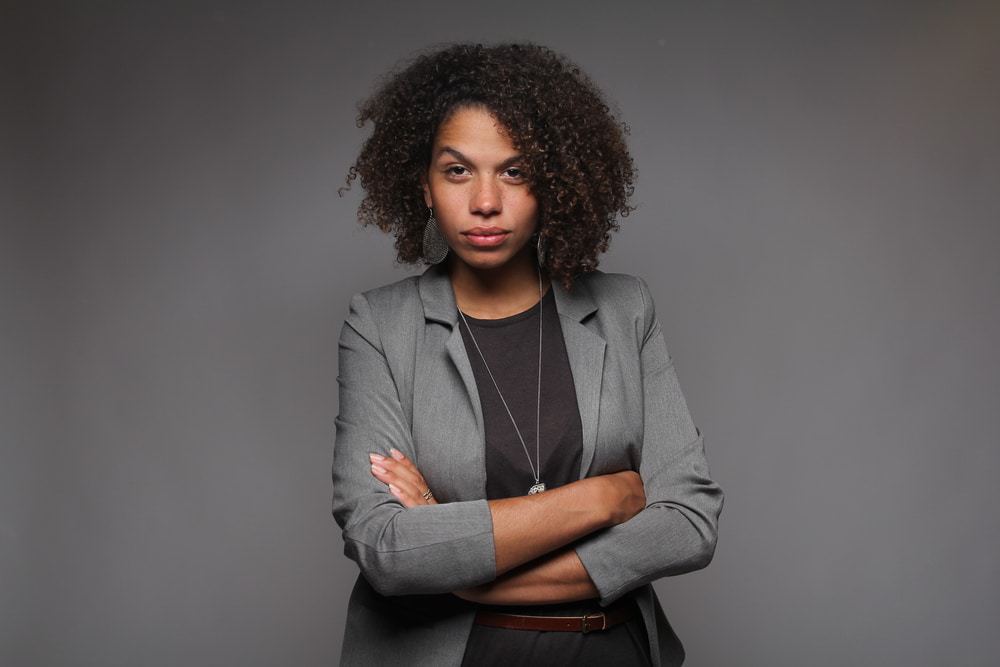 African American female with curly type 3b hair treated with safflower oil wearing a gray jacket and black shirt.