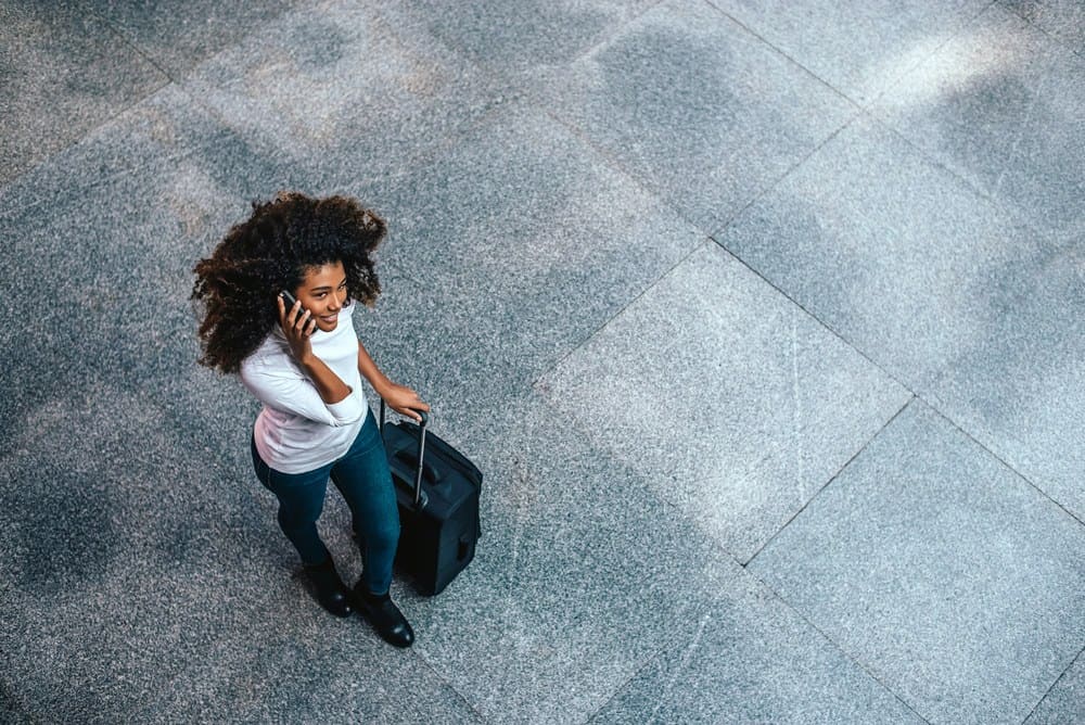 Top view of woman with type 3c curly hair carrying a trolley bag talking on phone as she prepares to board an airplane.