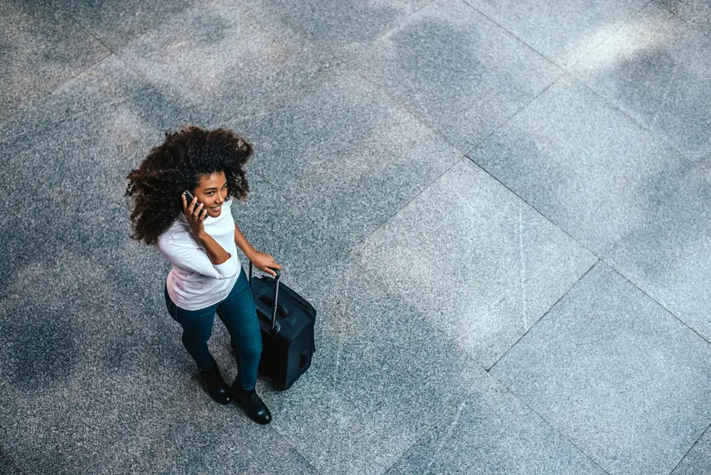 How to Use Thyme Oil for Hair Growth, Stress, Dry Scalp, and More 8 Top view of woman with type 3c curly hair carrying a trolley bag talking on phone as she prepares to board an airplane.