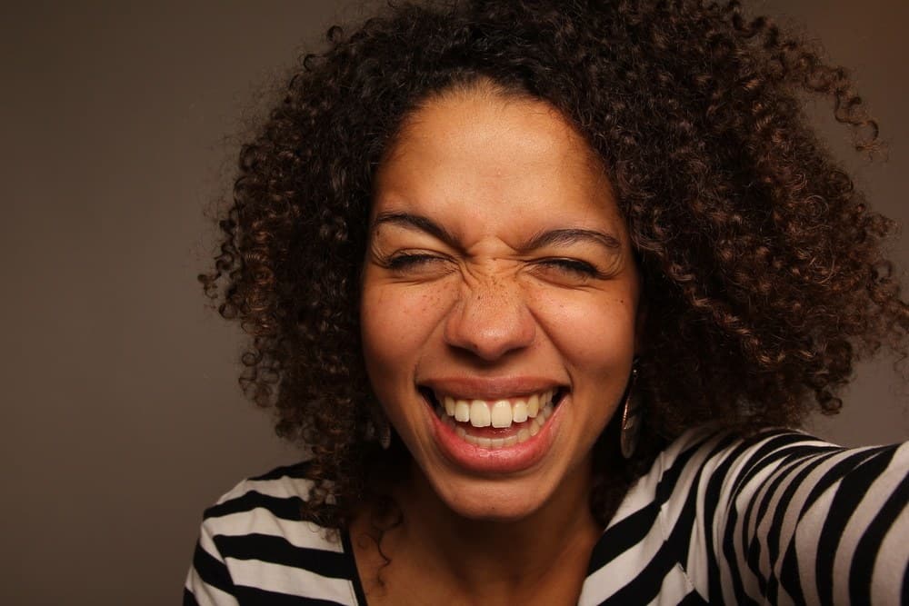 Cute light skinned black girl with curly hair smiling wearing a black and white striped shirt. 