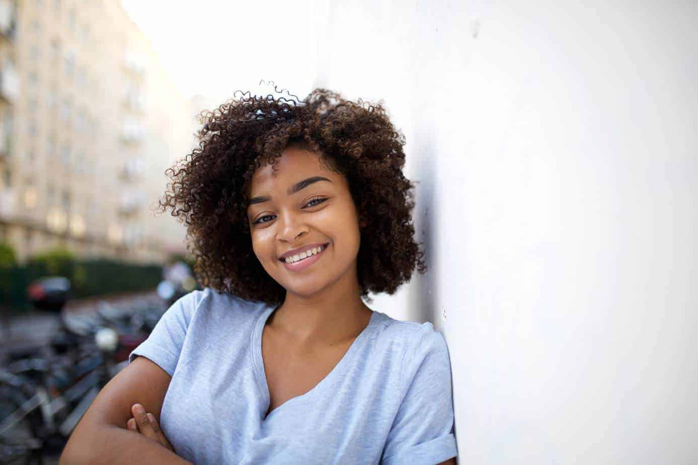 Cute young black girl leaning on a wall and smiling after using chebe powder after reading a quote from Uchenna Okereke.