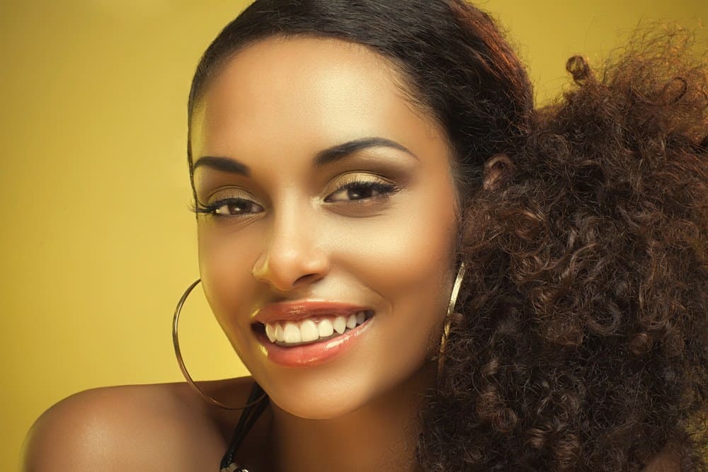 A beautiful portrait of African American woman wearing a curly pony tail on a honey blonde background.