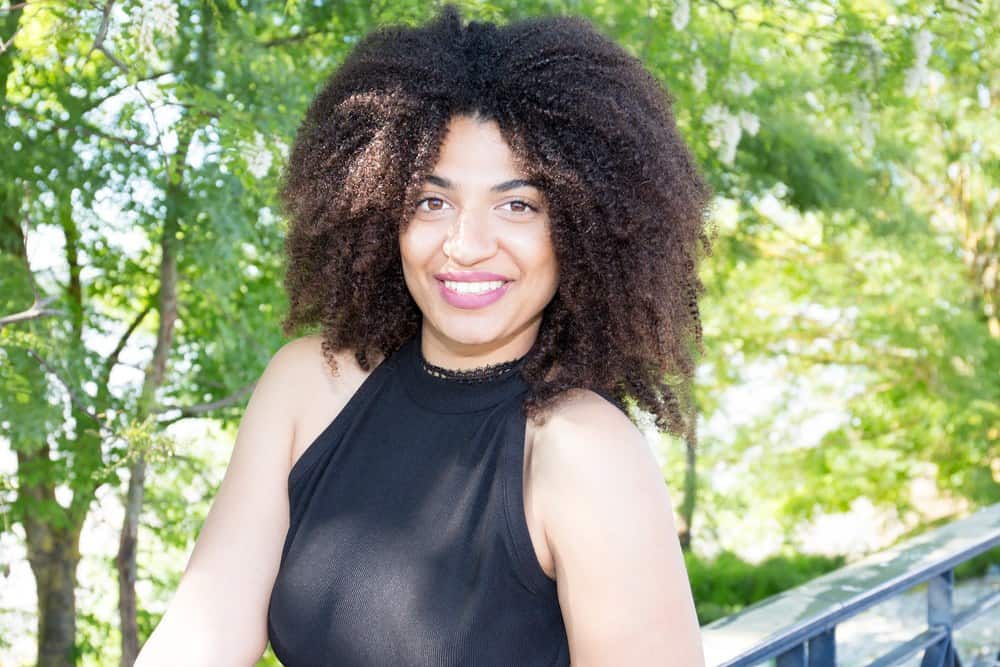 Pretty woman with natural hair afro posing outdoor in black dress after using lemongrass oil on her hair.