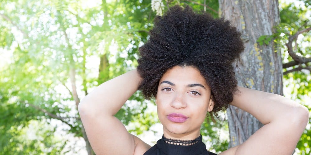 Cheerful mixed American girl outdoors holding her curly hair above her head, wearing pick lipstick.