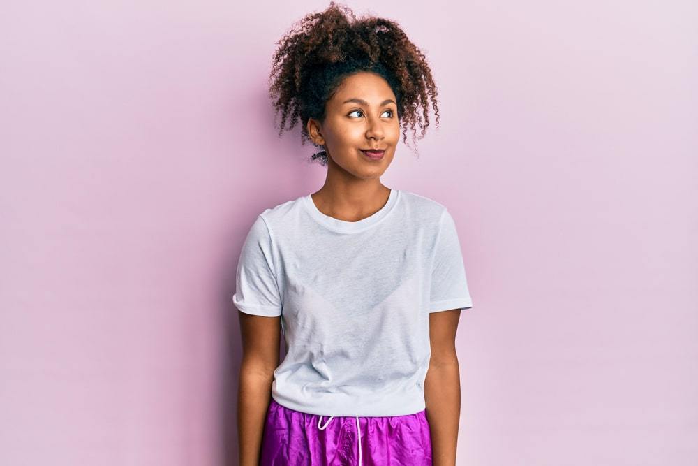 Beautiful African American woman with afro hair wearing sportswear smiling looking to the side and staring away thinking.