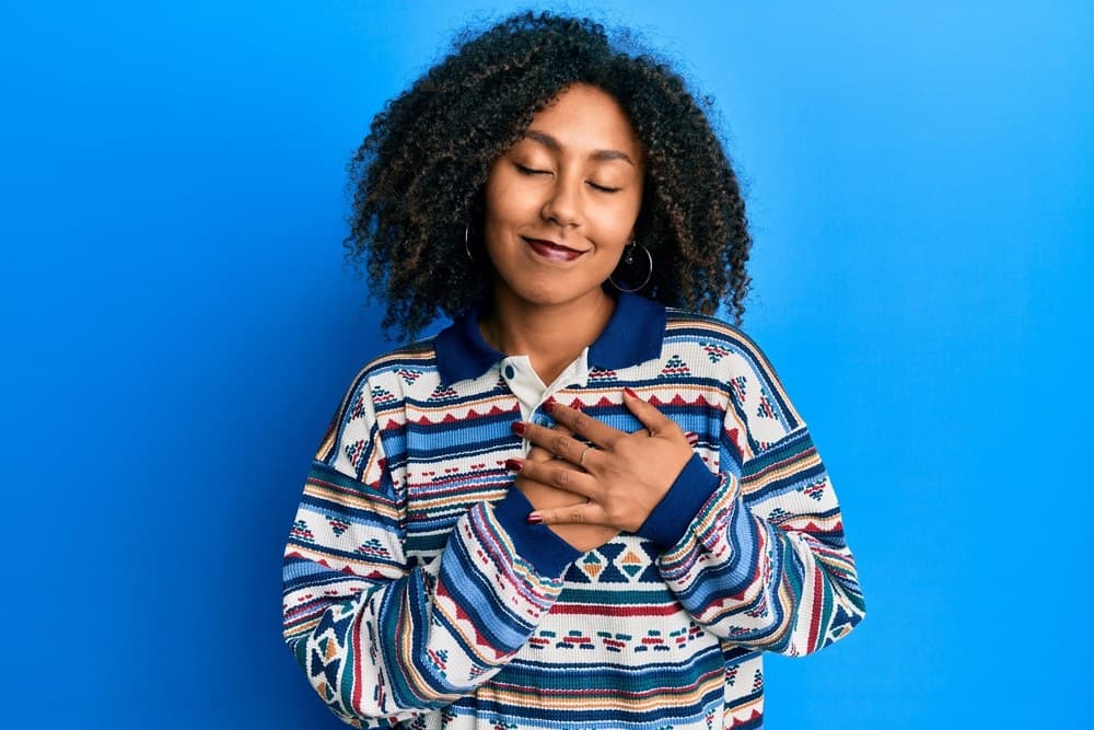 Beautiful African American woman with afro hair wearing casual clothes smiling with hands on chest, eyes closed with grateful gesture on face.